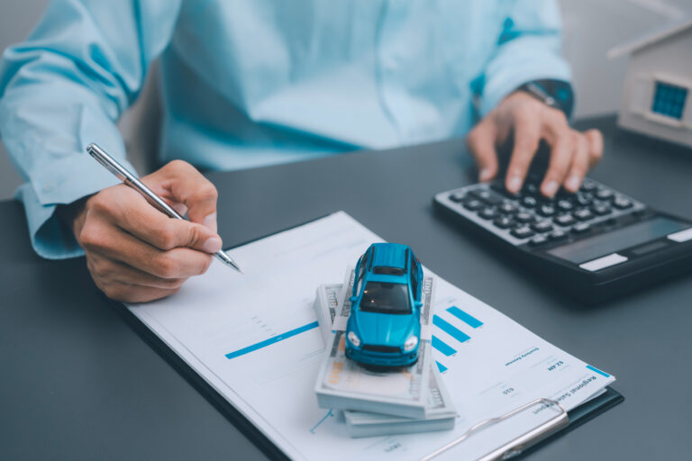 Auto loan vehicle leasing and car insurance concept business person hand signing contract document with pen near blue miniature car on stack of money cash and calculator