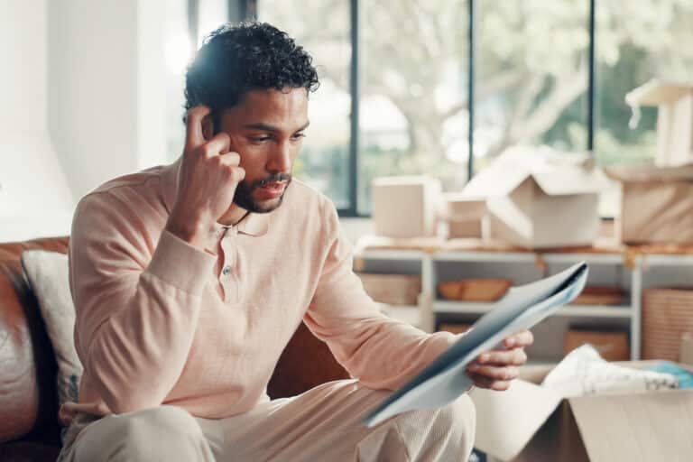 Moving, man or stress with documents in home for eviction notice, lease violation or finance crisis. Relocation, person or worry with paperwork on sofa for hidden foreclosure clause and rent pressure.